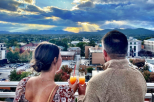 A couple on a rooftop cheersing cocktails while looking at a sunset
